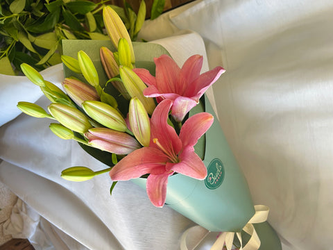 Bouquet of pink and yellow lily flowers with a green bottle in the background